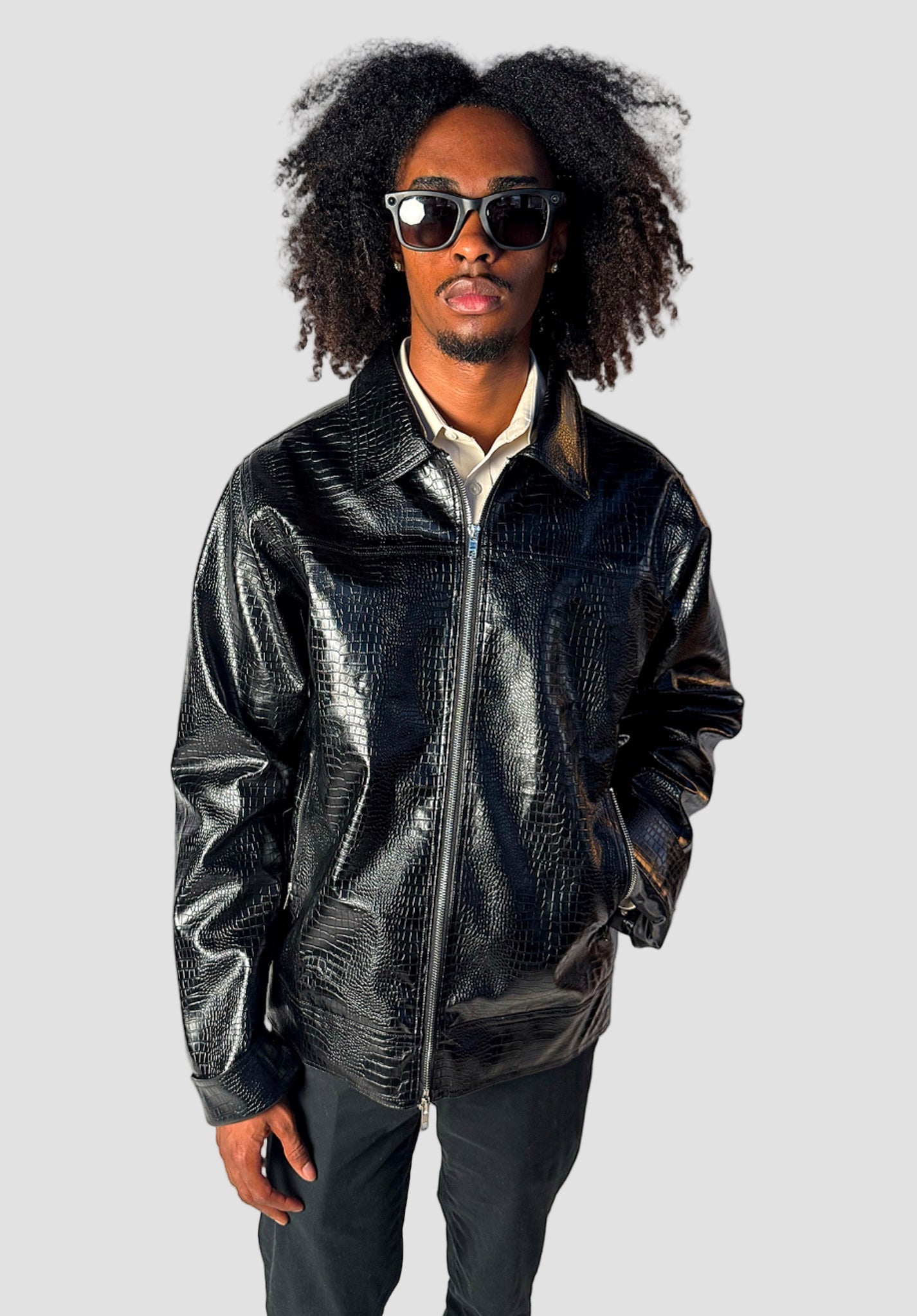 Person wearing a black leather jacket and sunglasses against a gray background